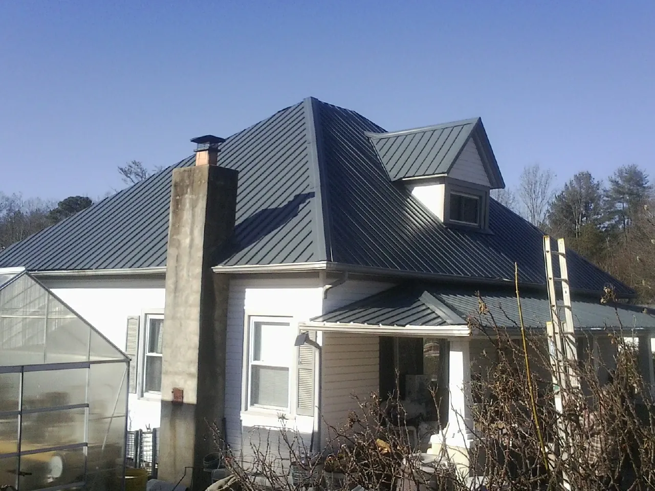 Dark blue standing seam metal roof on a white farmhouse with dormer — Slate & Tile Roof Repair by Roofing Brothers in Kernersville