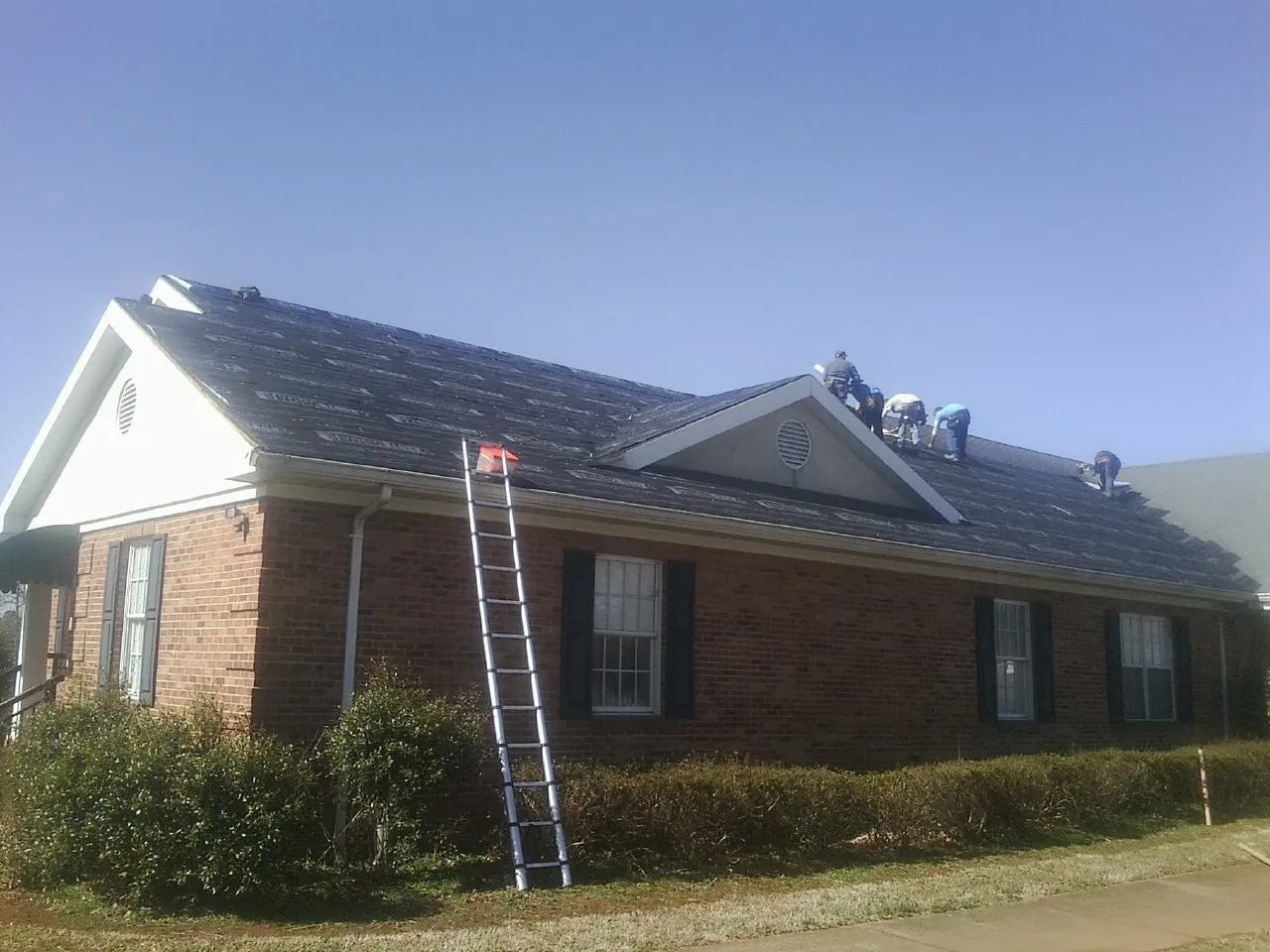 Crew tearing shingles off a brick ranch roof with a ladder set — Emergency Roof Repair work by our crew in Kernersville