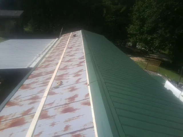 Old rusted panels beside newly installed green metal roofing — Wind Damage Roof Repair by Roofing Brothers in Kernersville