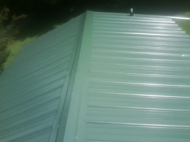 New green metal panels meeting at the ridge of a roof — Flat Roof Repair work by our crew in Kernersville