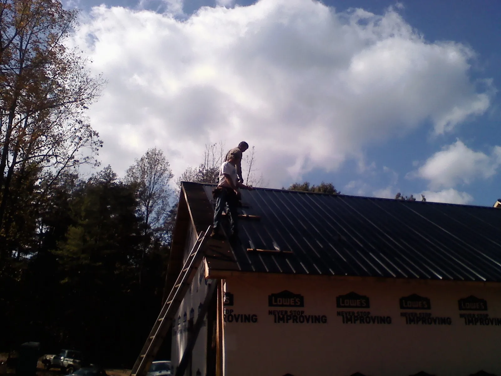 Roofer fastening dark metal panels high against a cloudy sky, from a Roof Inspection job in Kernersville