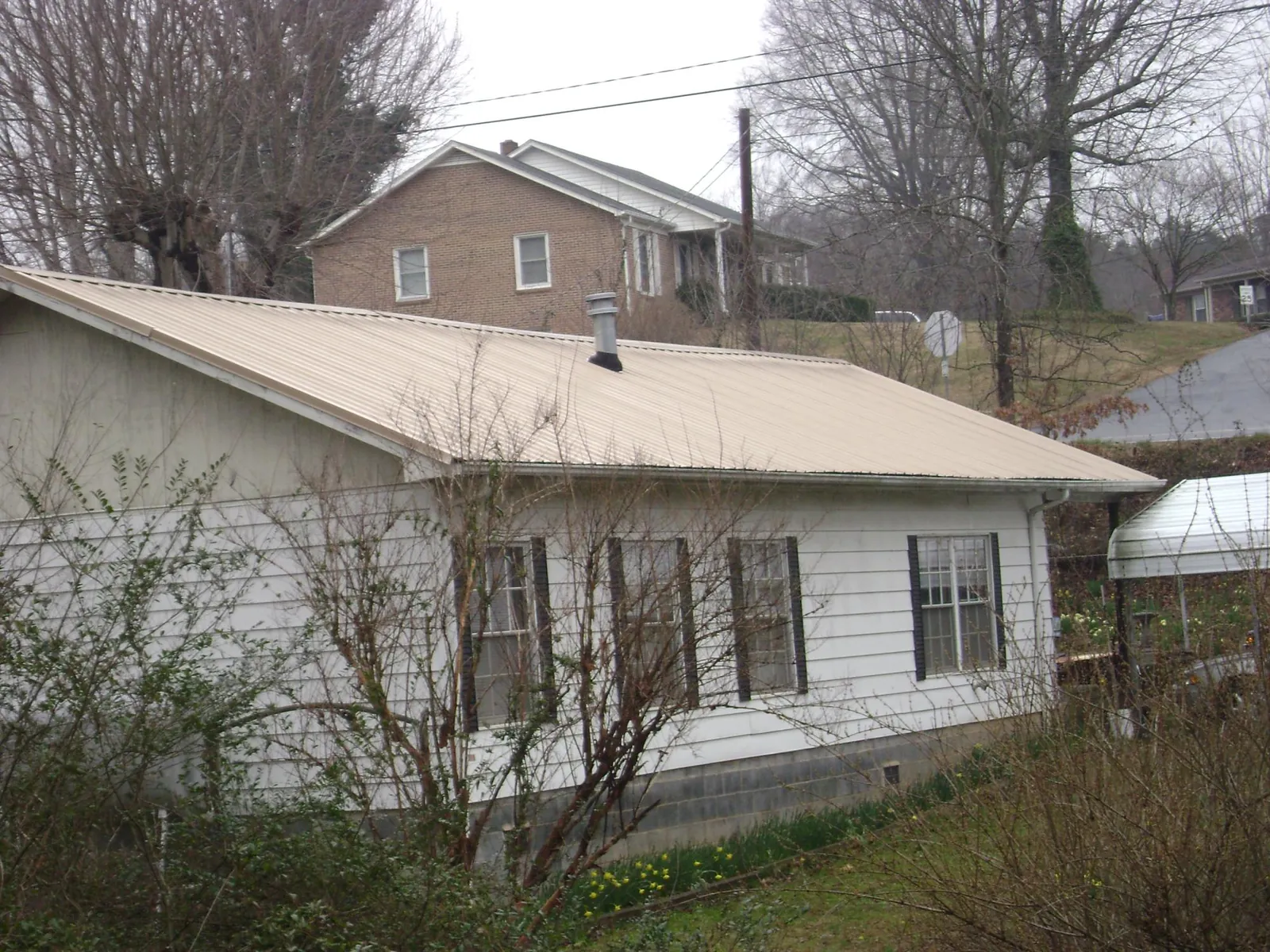 Tan metal roof on a white sided house set into a hillside — Commercial Roofing by Roofing Brothers in Kernersville