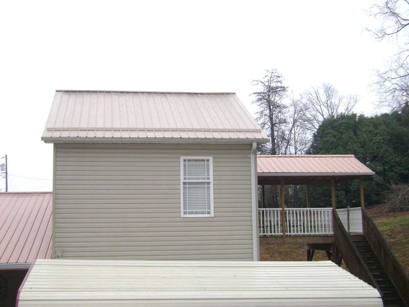 Tan metal roofs on a two story addition and attached porch, from a Roof Replacement job in Kernersville